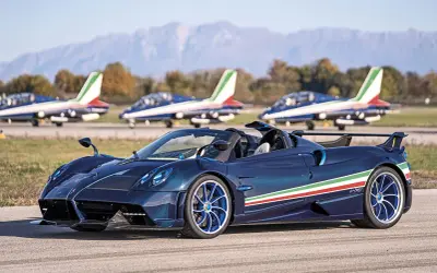 Niebieski Pagani Huayra Roadster z włoską flagą na boku, obok samolotów akrobacyjnych. Jego pagani huayra cena jest astronomiczna.