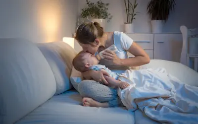 Matka karmi dziecko butelką w łóżku, czule całując je w czoło. Nawet koszmary senne nie są straszne, gdy czuwa kochająca mama.