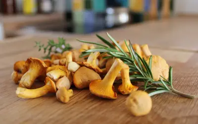 Un mucchio di finferli dorati, che dimostrano come i funghi sono verdure, con rametti di rosmarino su un tagliere di legno.