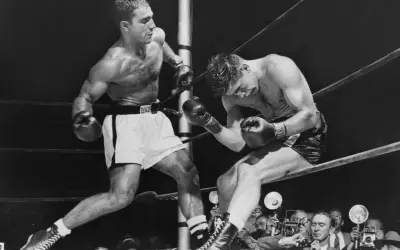Two boxers in a ring, one on the offensive. Rocky Marciano, who won all 49 of his professional fights, is depicted here.