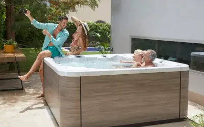 Un homme prend un selfie près d'un jacuzzi où deux couples profitent d'un moment de détente. L'entretien jacuzzi est essentiel pour ces instants de bonheur.