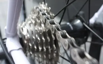Biała rama roweru, metalowy łańcuch i zębatki tworzą mechanizm wolnobiegu.