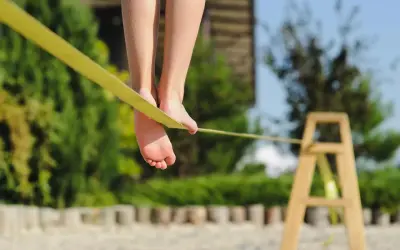 Füße balancieren auf einer gelben Slackline, die an einem Holzgestell befestigt ist.