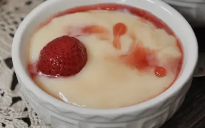 Aksamitna masa budyniowa z truskawką i malinowym sosem w białej miseczce.