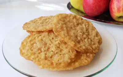 Tre gyllene glutenfria havreflarn ligger staplade på en glasfat. I bakgrunden syns äpplen och päron.