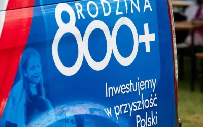 Niebieski baner z napisem "RODZINA 800+" i hasłem "Inwestujemy w przyszłość Polski". Widoczne uśmiechnięte dzieci.