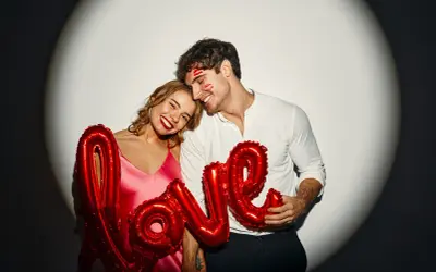 Para, z balonami "LOVE" i śladami pocałunków na twarzy, uosabia wzruszające do łez cytaty o miłości.
