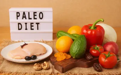 Na stole świeży kurczak, warzywa i owoce. Tablica z napisem "PALEO DIET" sugeruje zdrowe odżywianie.