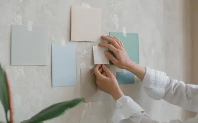 Händer arrangerar färgglada papper på en vägg. Tre tavlor bredvid varandra bildar en del av en moodboard.