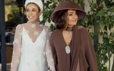 La madre de la novia, elegante con sombrero marrón, acompaña a la radiante novia con su vestido blanco adornado.