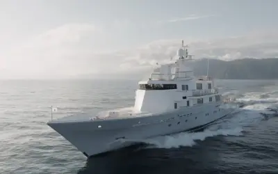 L'alessandro del bono yacht solca le onde con eleganza, un gioiello bianco su un mare calmo, con montagne sullo sfondo.