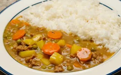 Un plat de riz blanc servi avec un curry japonais savoureux, garni de morceaux de carottes, de pommes de terre et de petits pois.