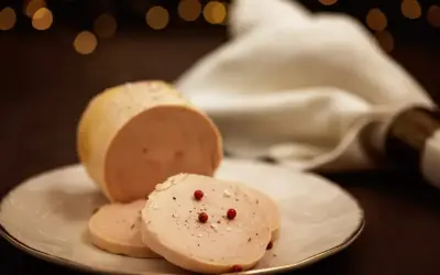 Tranche de foie gras, une des spécialités culinaires Dordogne, assaisonnée de poivre et de baies roses sur une assiette blanche.