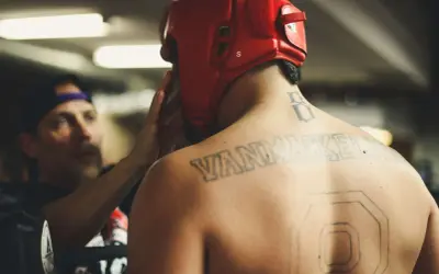 En fighter med röd hjälm och tatueringar på ryggen förbereds inför match. Kanske undrar du vad betyder MMA?