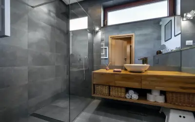 Salle de bain moderne avec douche à l'italienne, carrelage gris, meuble en bois, vasque et miroir. L'étanchéité de la douche italienne est assurée par un receveur discret.