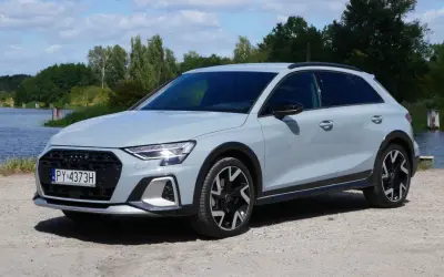 Jasnoszary Audi A3 allstreet stoi na żwirowej drodze nad jeziorem.