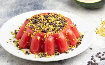 Delizioso gelo di anguria, guarnito con gocce di cioccolato e pistacchi tritati, su un piatto bianco.