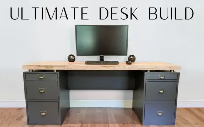 A modern DIY computer desk with a light wood top, dark gray drawers, and a monitor setup.