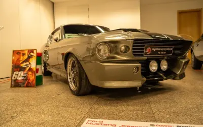 Szary Ford Mustang „Eleanor” z filmu „60 sekund” obok plakatu z Nicolasem Cage'em.