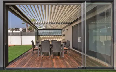 Porches cerrados con encanto, con mesa y sillas de mimbre sobre tarima de madera y césped artificial.