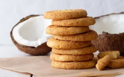 Stos ciastek z mąki kokosowej, obok połówki kokosa. Idealne na deser.