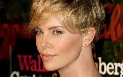 Charlize Theron w fryzurze pixie, która dodaje objętości cienkim włosom, z subtelnym makijażem i złotą biżuterią.