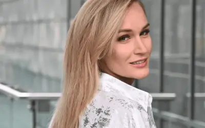 Uśmiechnięta Kamila Boś, w białej koszuli z wzorem, patrzy przez ramię.
