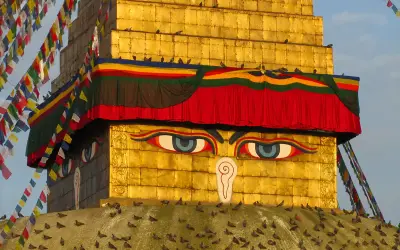 Złota stupa z oczami Buddy, ozdobiona kolorowymi flagami modlitewnymi. Warto odwiedzić takie miejsca święte w buddyzmie w Nepalu i Indiach.