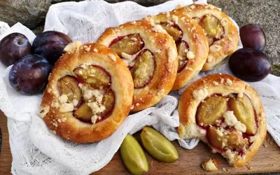 Pyszne drożdżówki ze śliwką, posypane kruszonką, prezentują się apetycznie obok świeżych śliwek.