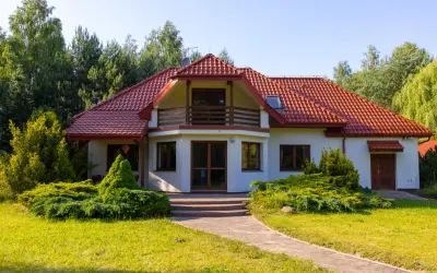 Urokliwa agroturystyka w dolinie stawów. Biały dom z czerwoną dachówką, otoczony zielenią, zaprasza na wypoczynek.