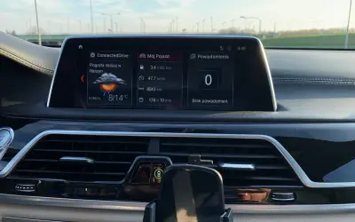Wnętrze BMW hybryda: ekran z pogodą w Raszynie (8/14°C), spalaniem 3.4l/100km i przebiegiem 8043km.