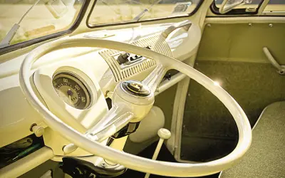Wnętrze klasycznego VW T1. Biała kierownica, deska rozdzielcza i zielona tapicerka.