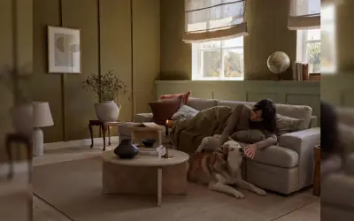 Gemütliches Wohnzimmer in warmen Farben. Eine Frau kuschelt mit ihrem Hund auf dem Sofa, umgeben von erdigen Tönen und sanftem Licht.