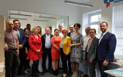 Grupa ludzi w eleganckich strojach pozuje do zdjęcia w biurze.
