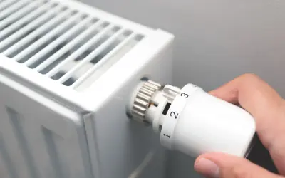 Dłoń kręci termostatem grzejnika, ustawiając temperaturę. Czas zacząć sezon grzewczy.