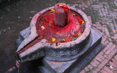 Kamienna podstawa z rynienką, na niej czerwony, ozdobiony kwiatami lingam, symbolizujący boga Śiwę.