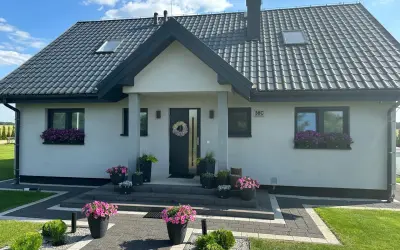 Nowoczesny dom z kamiennymi elementami, piękne kwiaty przed wejściem. Koszty budowy takiego domu mogą być różne.