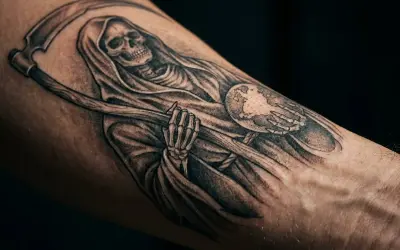 Chicano tattoo: Śmierć z kosą trzymająca kulę ziemską, symbolizująca przemijanie i los.