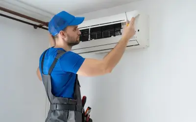 Technik w niebieskiej czapce i ogrodniczkach naprawia klimatyzator.