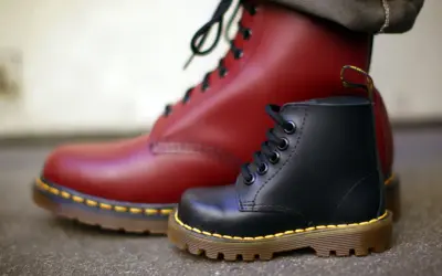 Ein roter und ein schwarzer Dr. Martens Stiefel, die die lange **Dr. Martens Geschichte** von robusten Schuhen für alle Generationen symbolisieren.