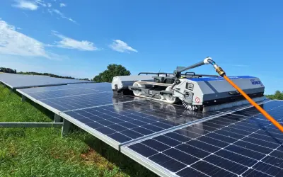 Robot do mycia paneli fotowoltaicznych czyści rzędy paneli na zielonej łące pod błękitnym niebem.