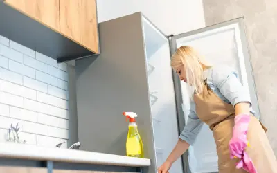 Kobieta w fartuchu i różowych rękawiczkach sprząta lodówkę, przygotowując się do usunięcia zapachów z lodówki.