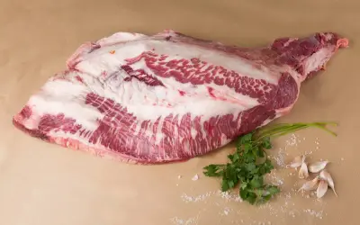 Un corte de carne cruda, con grasa marmoleada, listo para convertirse en un delicioso pastrami que es. Acompañado de perejil y ajos.