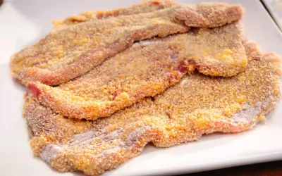 Mehrere panierte Schnitzel liegen auf einem weißen Teller, bereit für ein köstliches Schnitzel Rezept.