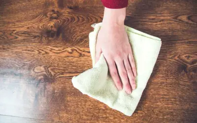 Mano limpiando un suelo de madera con un paño, aprendiendo como quitar manchas de la madera sin dañarla.