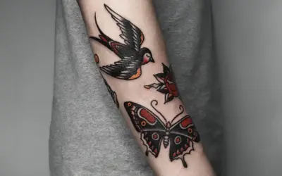 Tatuaż w stylu old school na przedramieniu: jaskółka, motyl i róża.