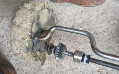Zestaw naprawczy przekładni napędu kosiarki z zabrudzonym kołem i elementami mechanizmu.