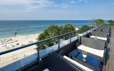 Wygodne fotele i stoliki na tarasie z widokiem na piaszczystą plażę i błękitne morze. Idealne miejsce na relaks, gdy dostępne są wolne pokoje z widokiem na morze.