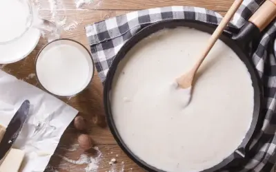 Gładki sos beszamel w patelni, obok mleko, masło i mąka.