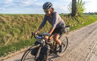 Kobieta w kasku i okularach przeciwsłonecznych jedzie na rowerze po piaszczystej drodze. To przygoda z rowerem w okolicach Gdańska.